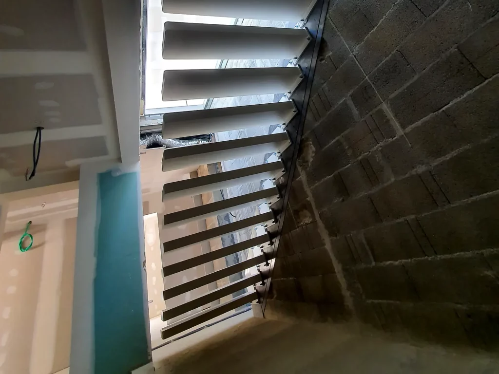Vue de dessous de la structure d’un escalier suspendu en acier en cours d’installation à Ventabren.